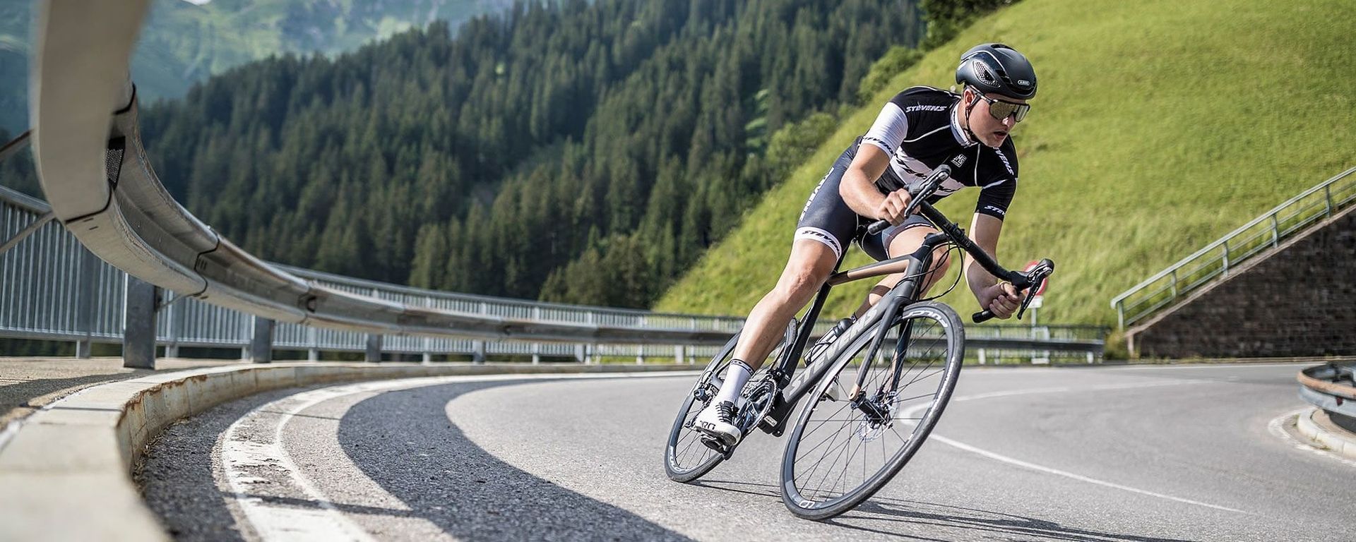 Rennradfahrer fährt auf kurviger Bergstraße in alpiner Landschaft